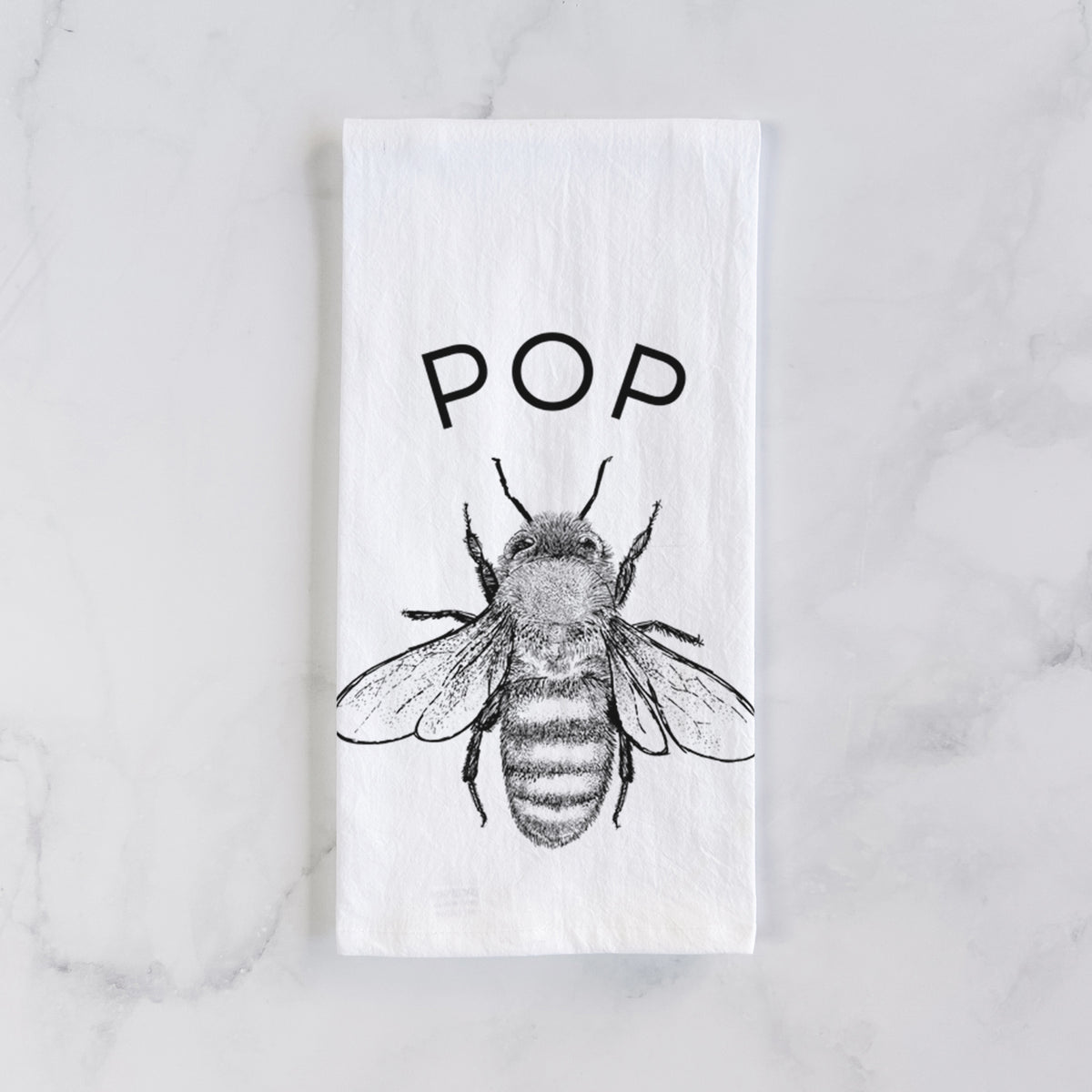 White cotton tea towel laid flat on marble, printed with a black ink honey bee beneath the word Pop.