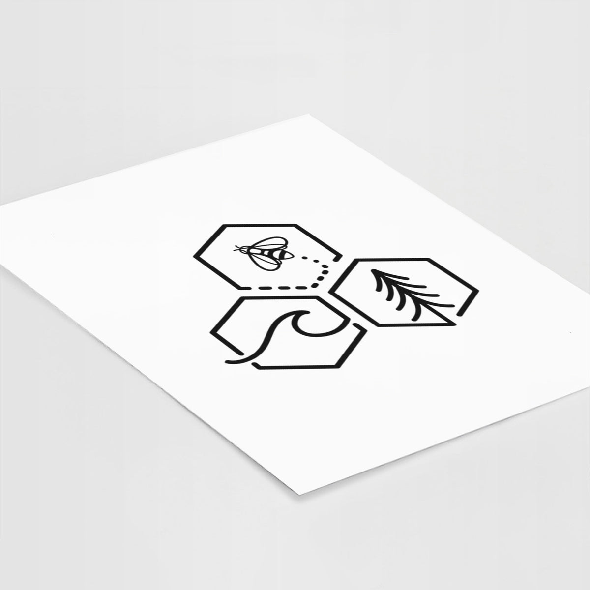 Art print of a black line art design of three hexagons holding a bee, an ocean wave and a pine tree, lying at an angle on a white surface.
