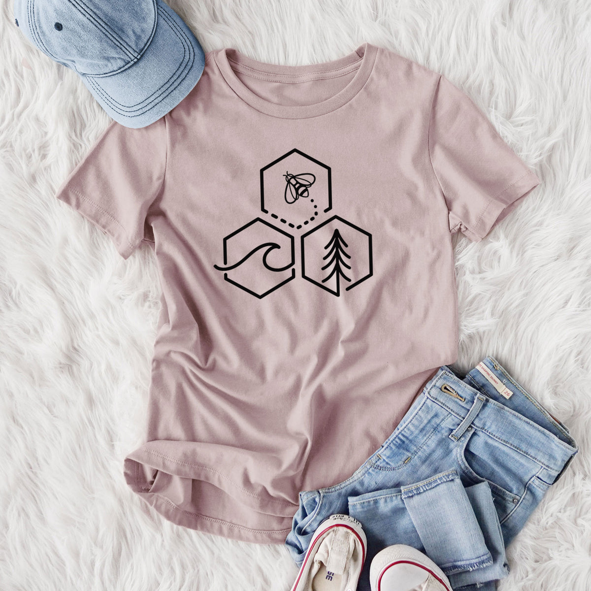 Women's relaxed fit cotton t-shirt printed with a black line art design of three hexagons holding a bee, an ocean wave and a pine tree, styled flat on a white faux fur rug with jeans.