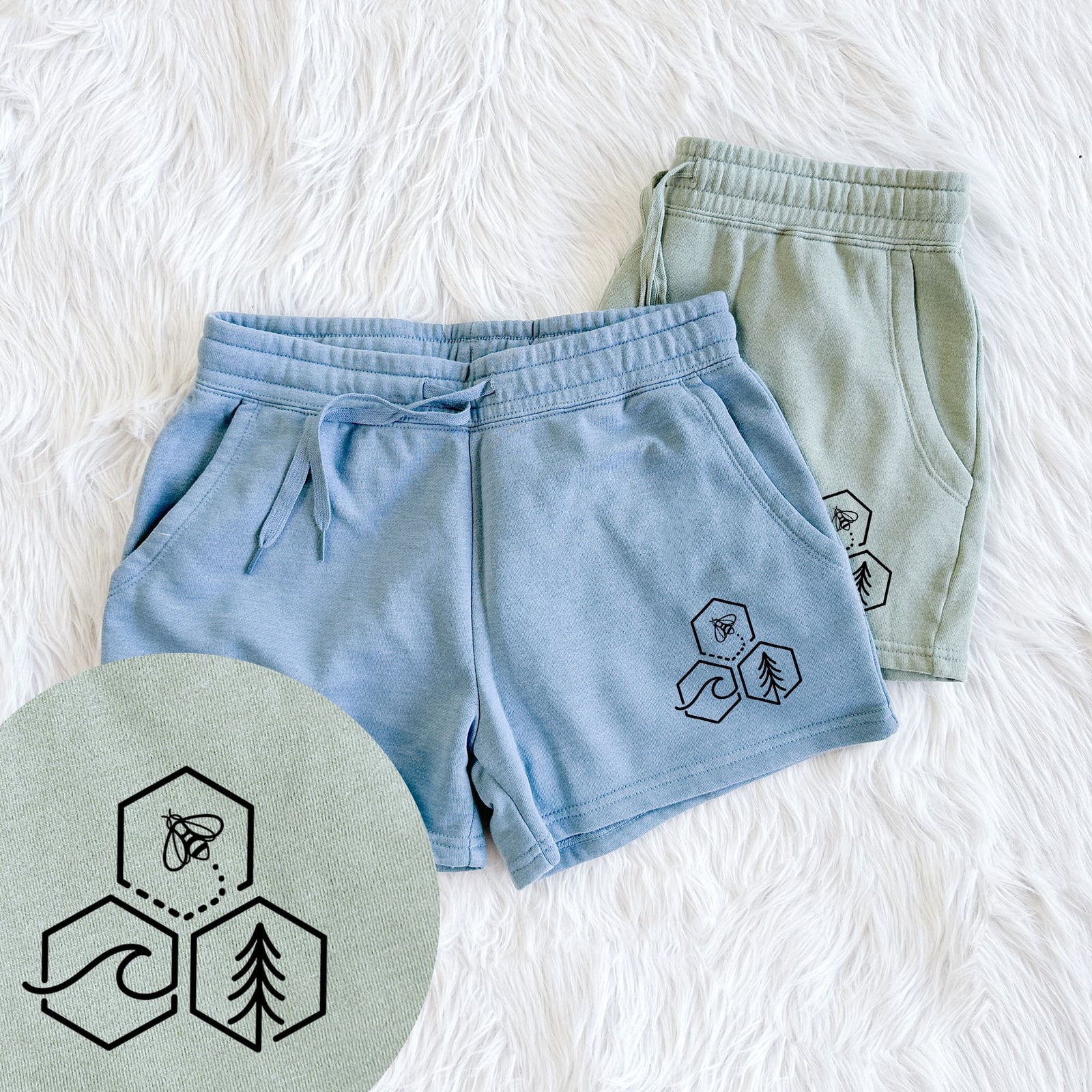 Two pairs of Cali Wave shorts in different colors printed with a black line art design of three hexagons holding a bee, an ocean wave and a pine tree, with a close-up of the print.