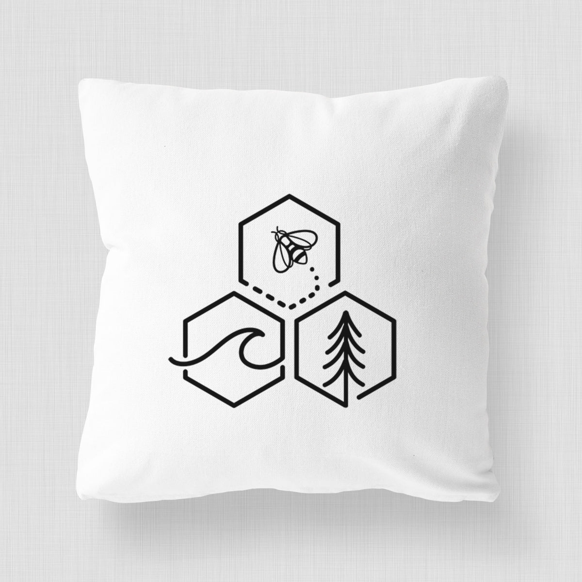 White pillow cover printed with a black line art design of three hexagons holding a bee, an ocean wave and a pine tree.