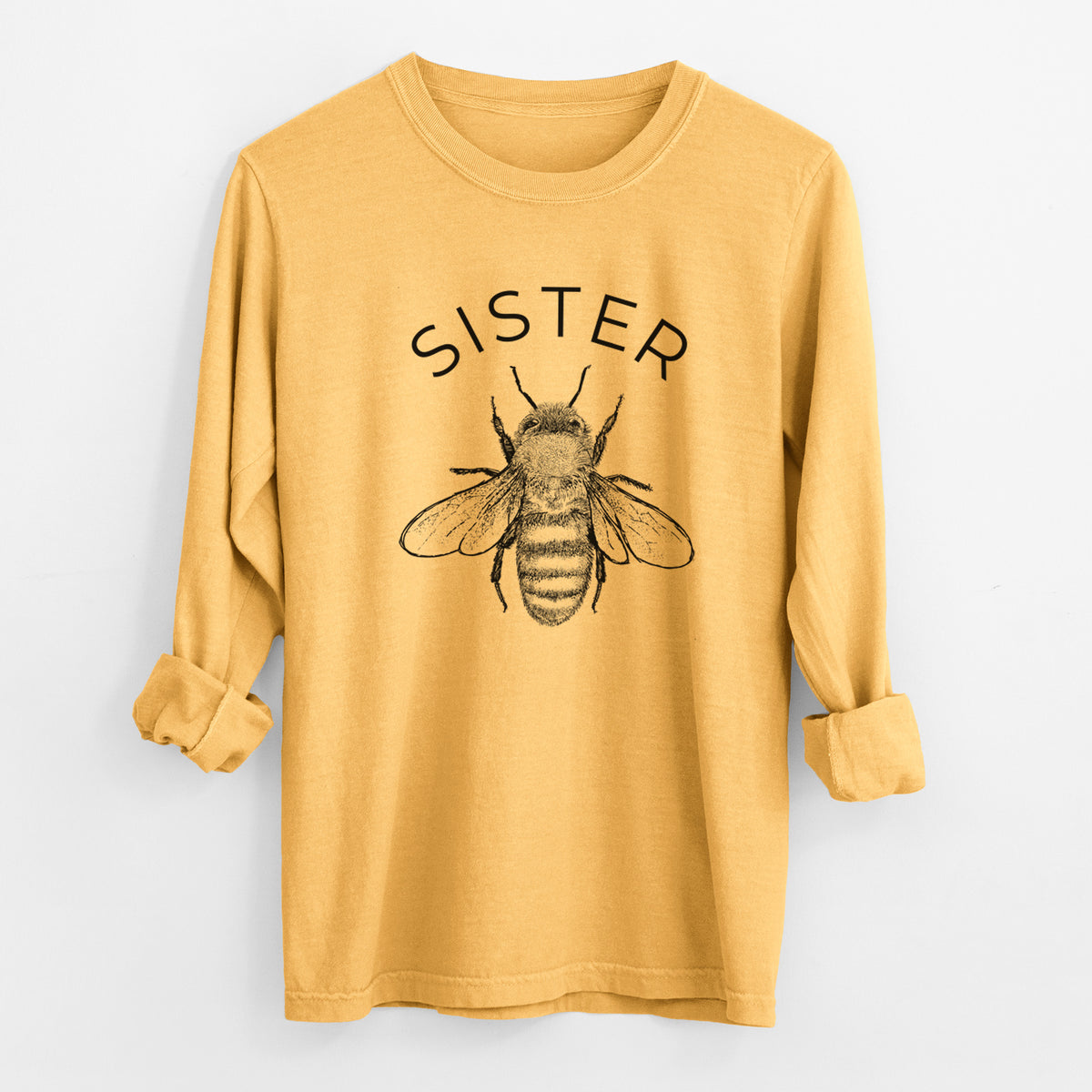 Golden wheat yellow Comfort Colors long sleeve shirt laid flat with the cuffs rolled, printed with a black ink honey bee beneath the word Sister.