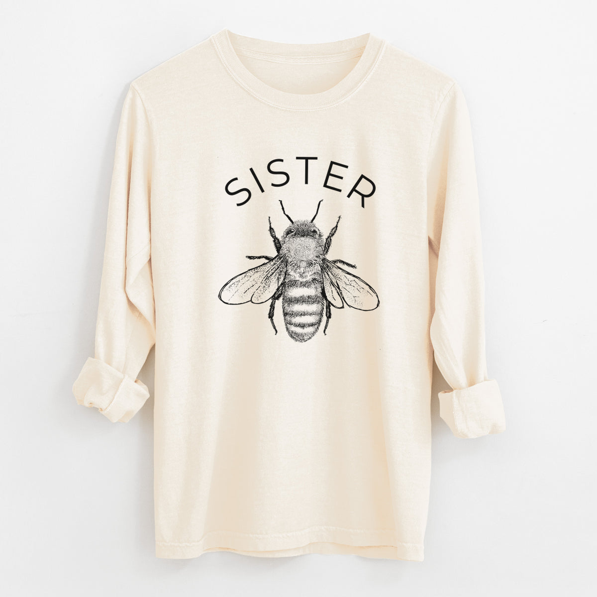 Ivory Comfort Colors long sleeve shirt laid flat with the cuffs rolled, printed with a black ink honey bee beneath the word Sister.