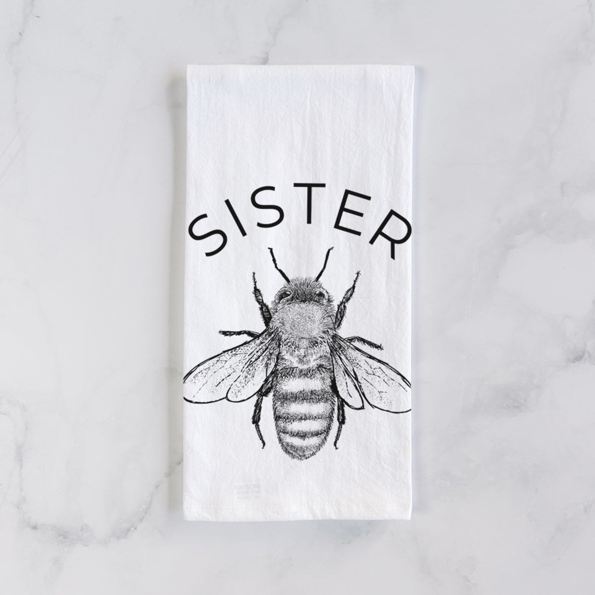 White cotton tea towel laid flat on marble, printed with a black ink honey bee beneath the word Sister.