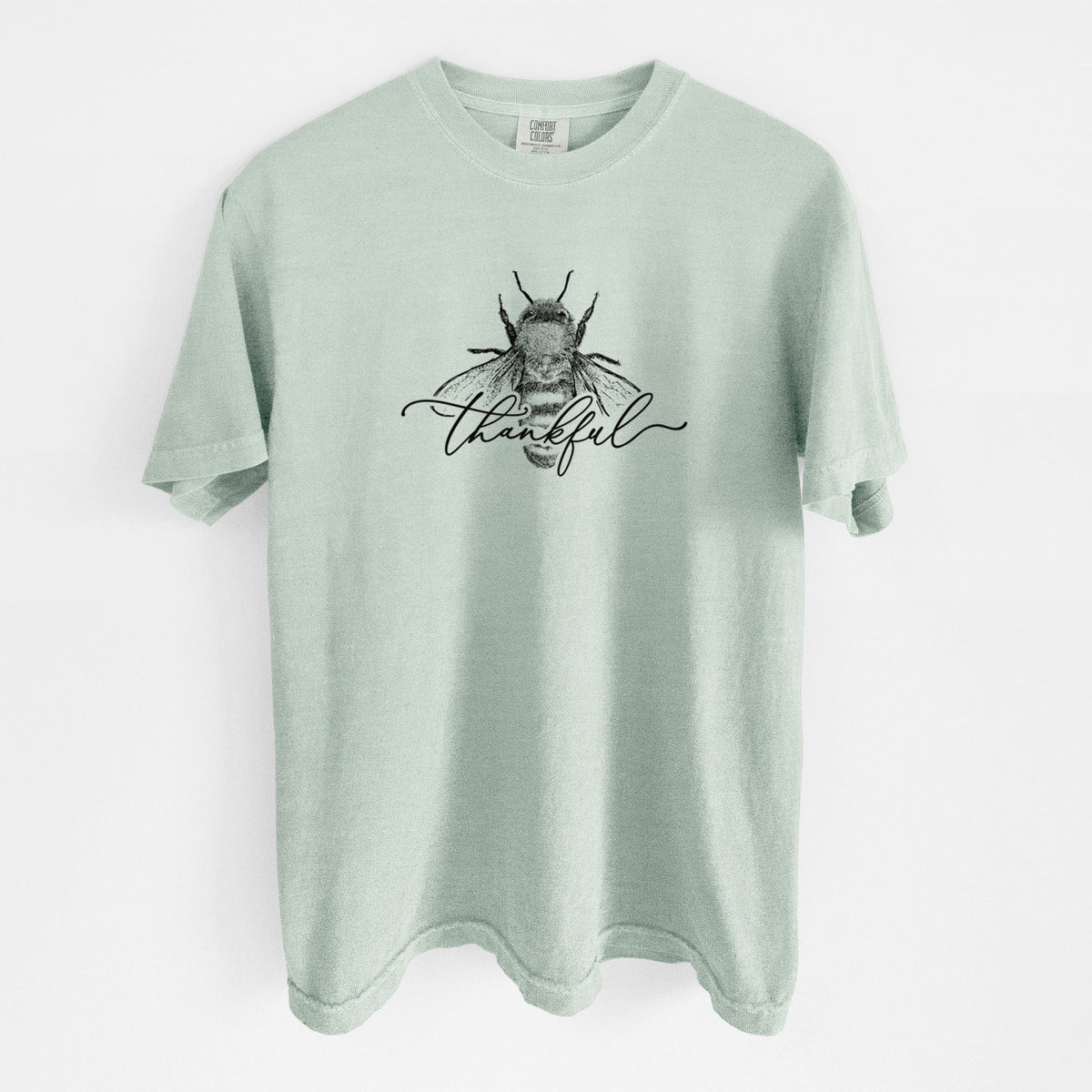 Bay green Comfort Colors t-shirt laid flat, printed with a black ink bee with the word thankful written in script across it.
