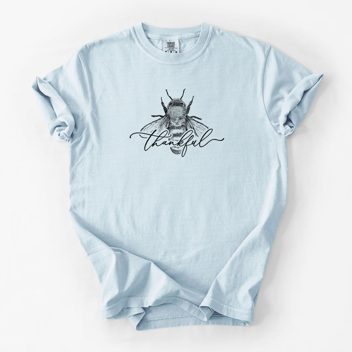 Chambray blue Comfort Colors t-shirt laid flat, printed with a black ink bee with the word thankful written in script across it.