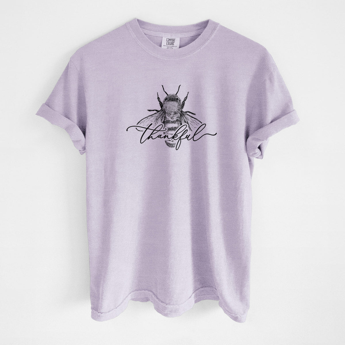 Orchid purple Comfort Colors t-shirt laid flat, printed with a black ink bee with the word thankful written in script across it.