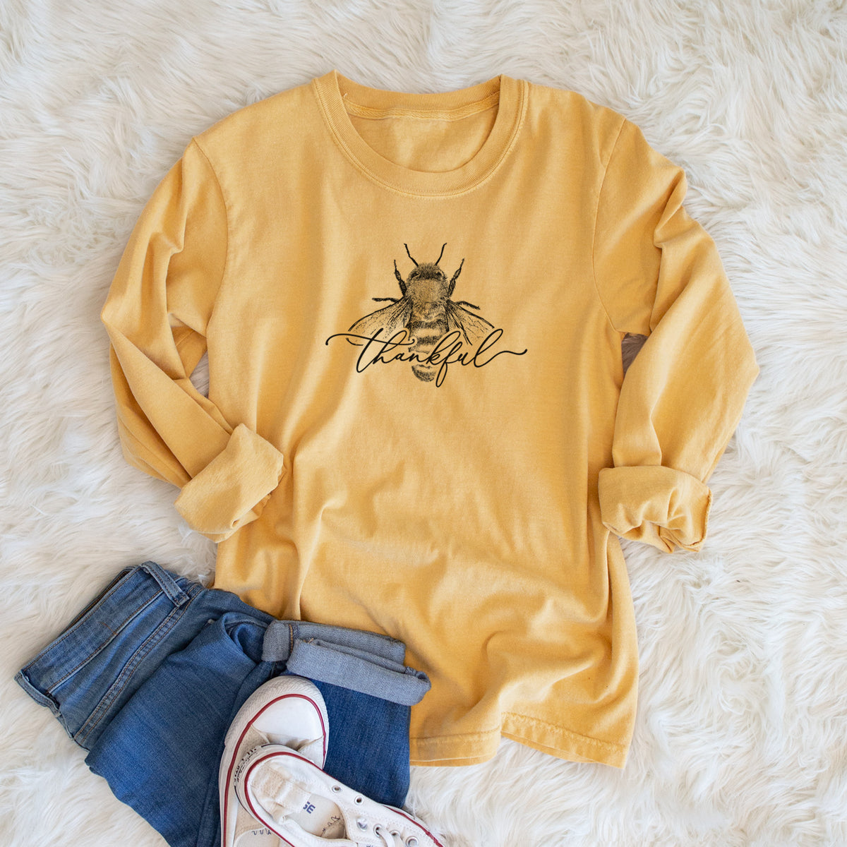 Golden wheat yellow Comfort Colors long sleeve shirt printed with a black ink bee with the word thankful written in script across it, shown in a lifestyle photo.