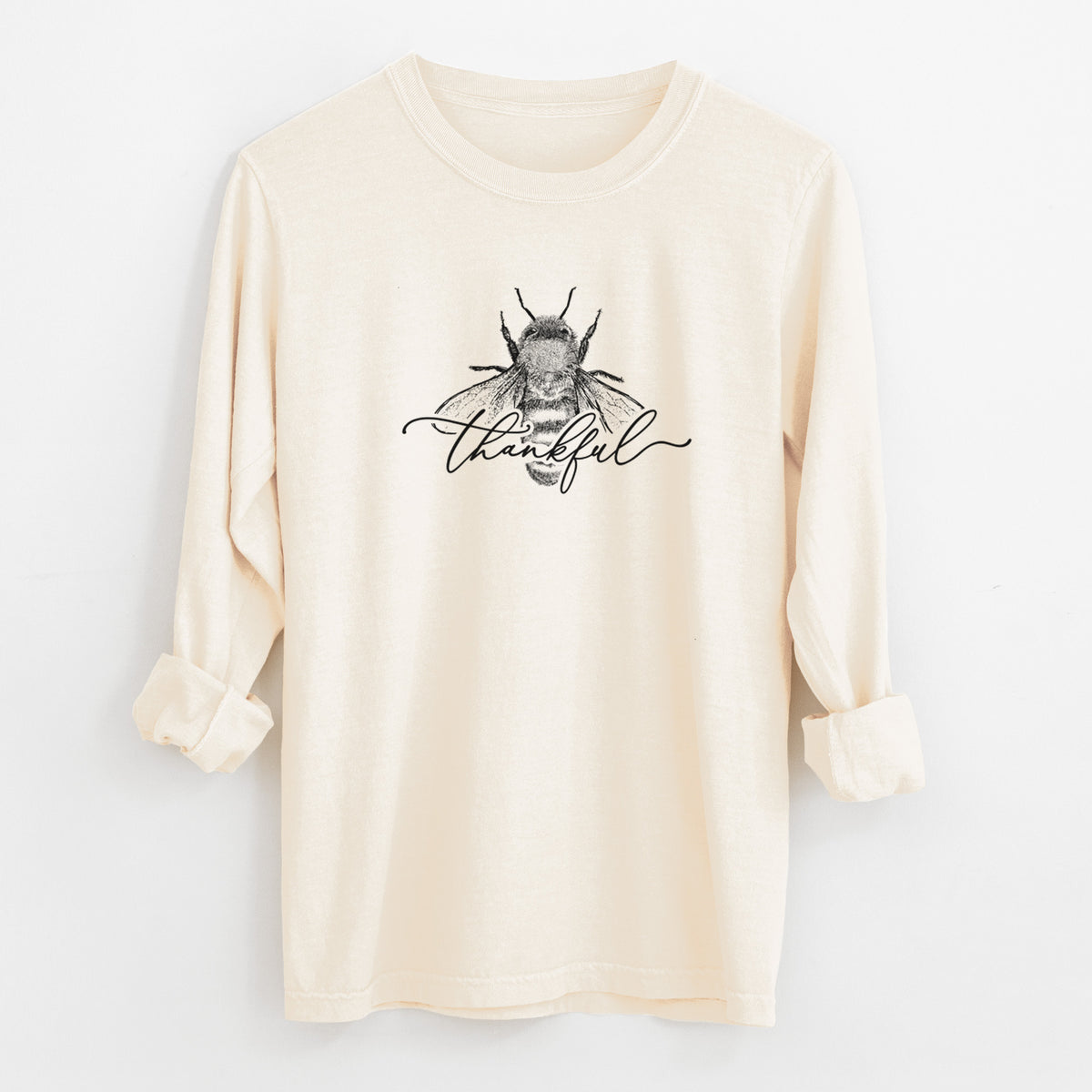 Ivory Comfort Colors long sleeve shirt laid flat with the cuffs rolled, printed with a black ink bee with the word thankful written in script across it.