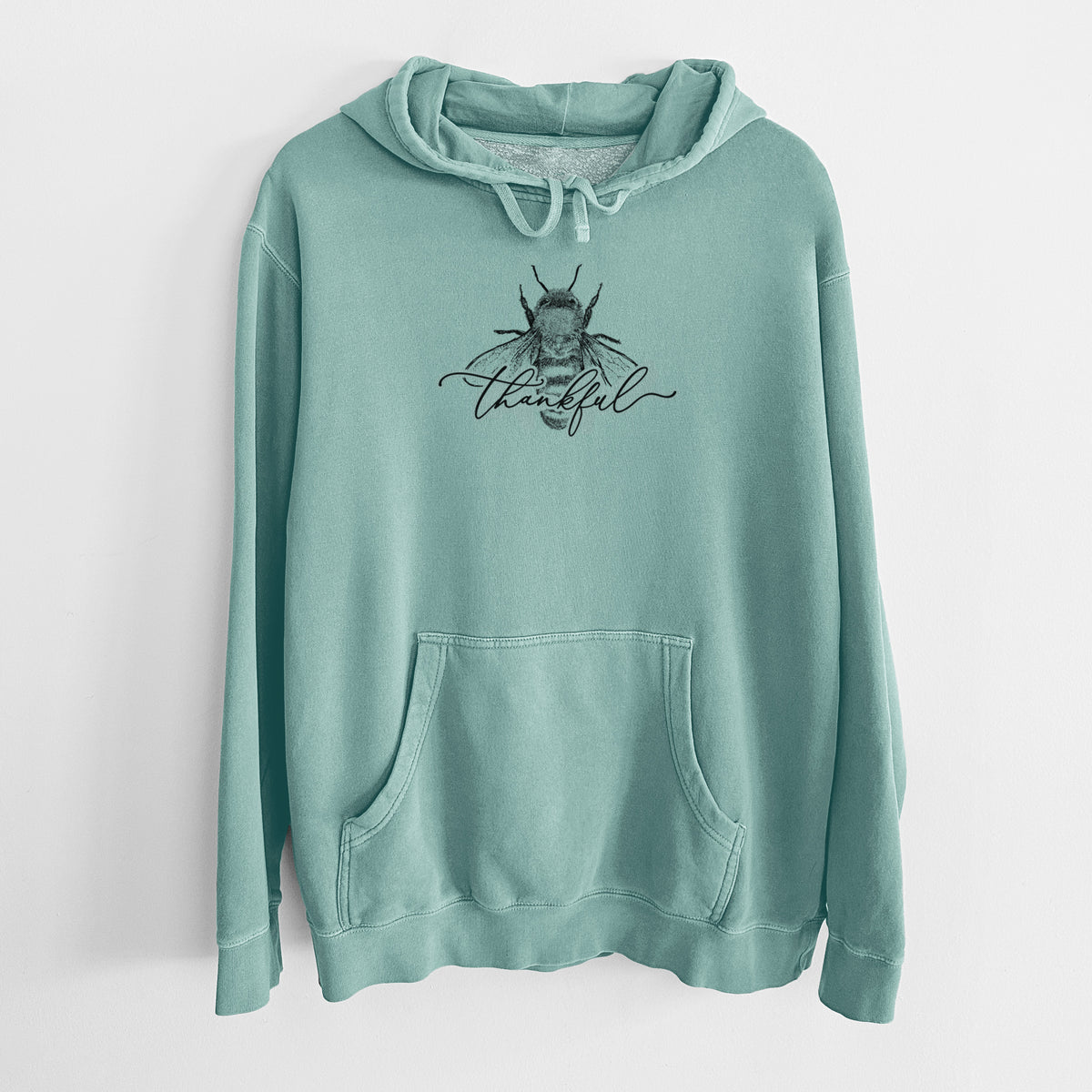 Mint green pigment dyed hoodie laid flat, printed with a black ink bee with the word thankful written in script across it.