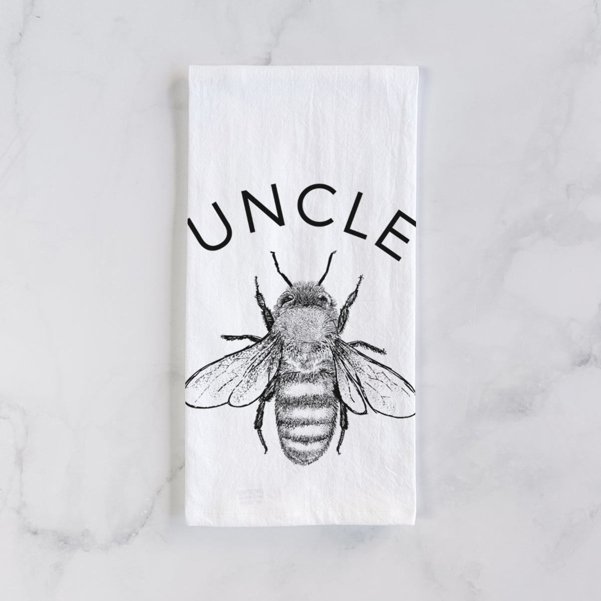 White cotton tea towel laid flat on marble, printed with a black ink honey bee beneath the word Uncle.