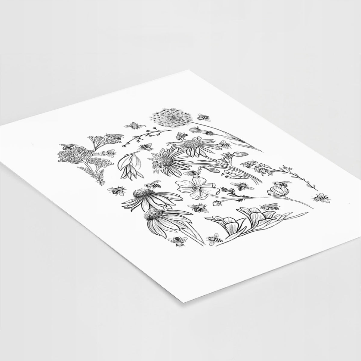 Art print of black ink bees scattered among wildflowers, lying at an angle on a white surface.