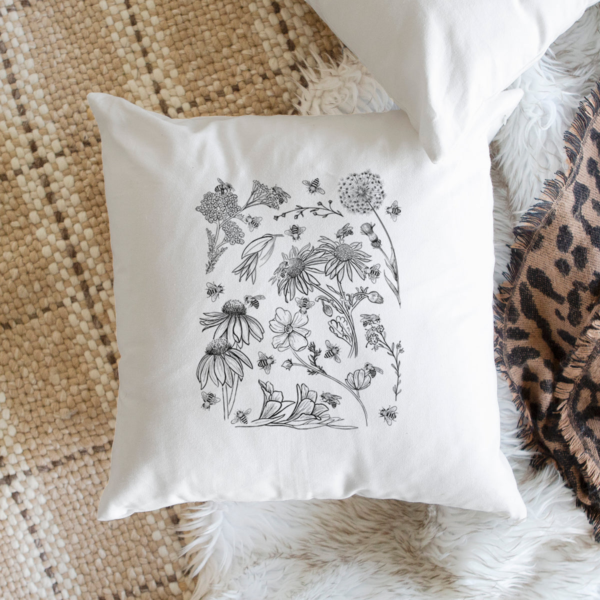 White pillow cover printed with black ink bees scattered among wildflowers, on a woven chair.