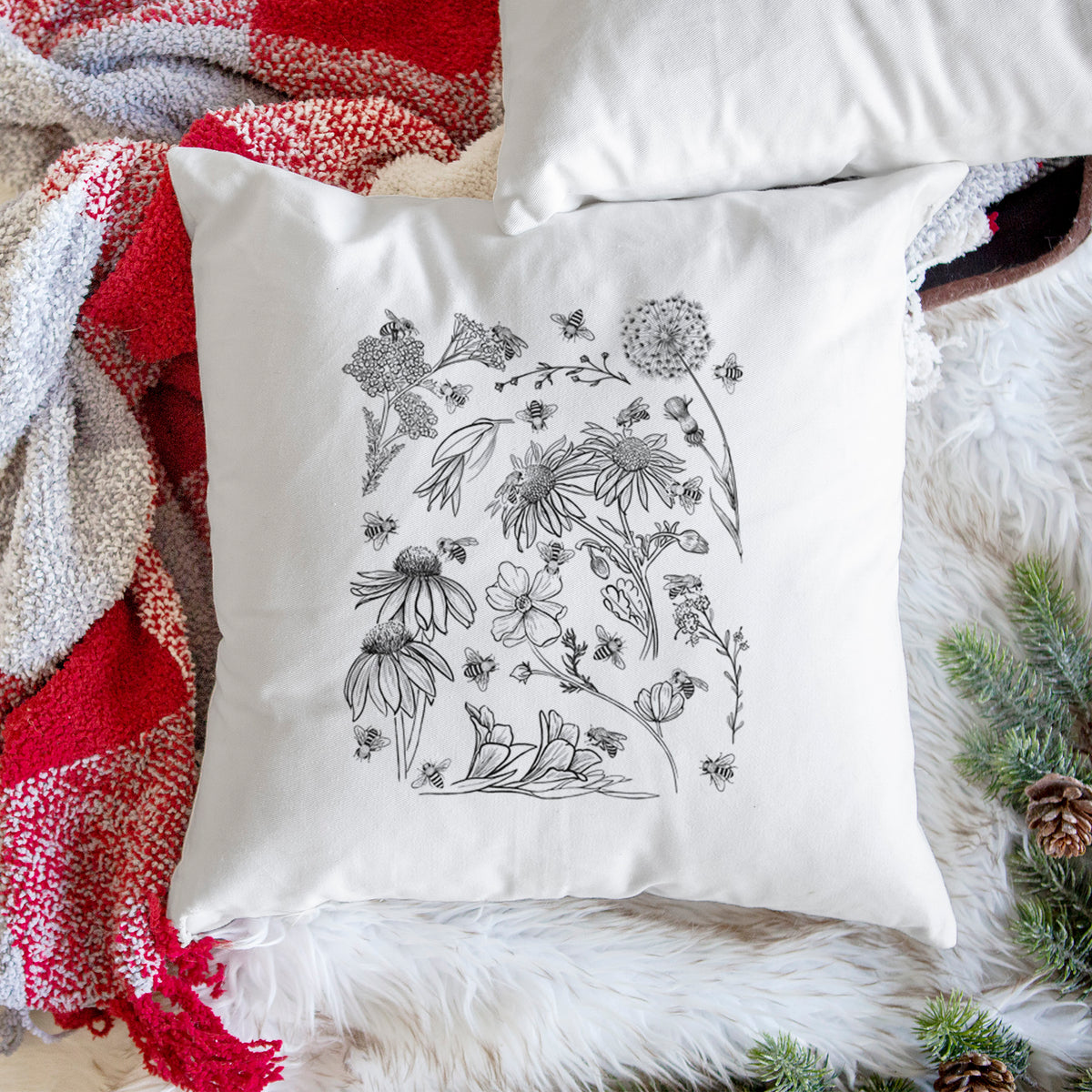 White pillow cover printed with black ink bees scattered among wildflowers, on a woven chair.