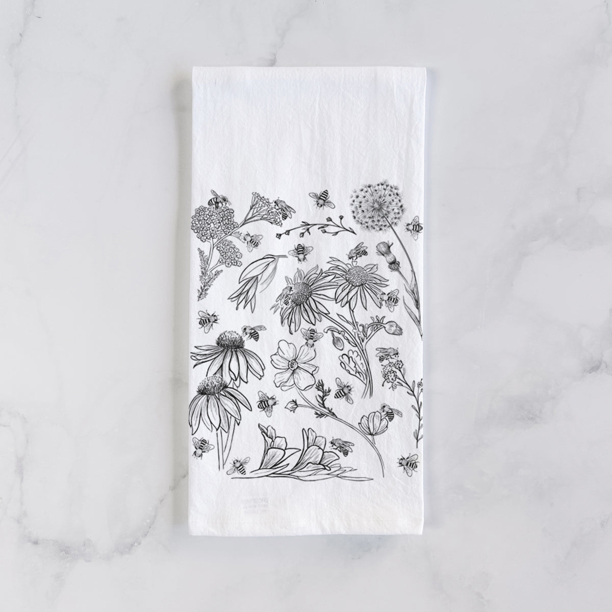 White cotton tea towel laid flat on marble, printed with black ink bees scattered among wildflowers.