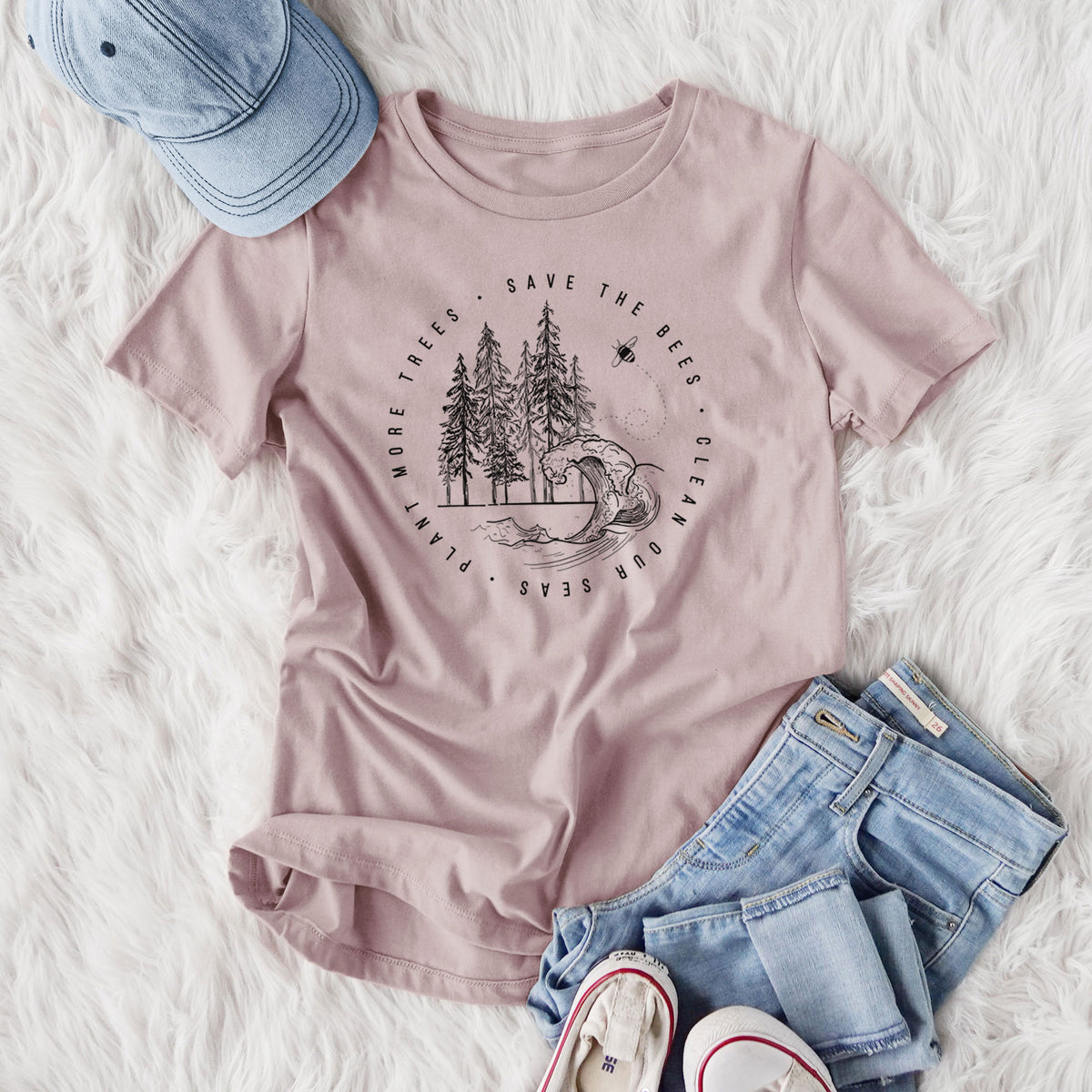 Women's relaxed fit cotton t-shirt printed with a circle of pine trees and an ocean wave ringed by the words Save the Bees, Clean Our Seas, Plant More Trees, styled flat on a white faux fur rug with jeans.