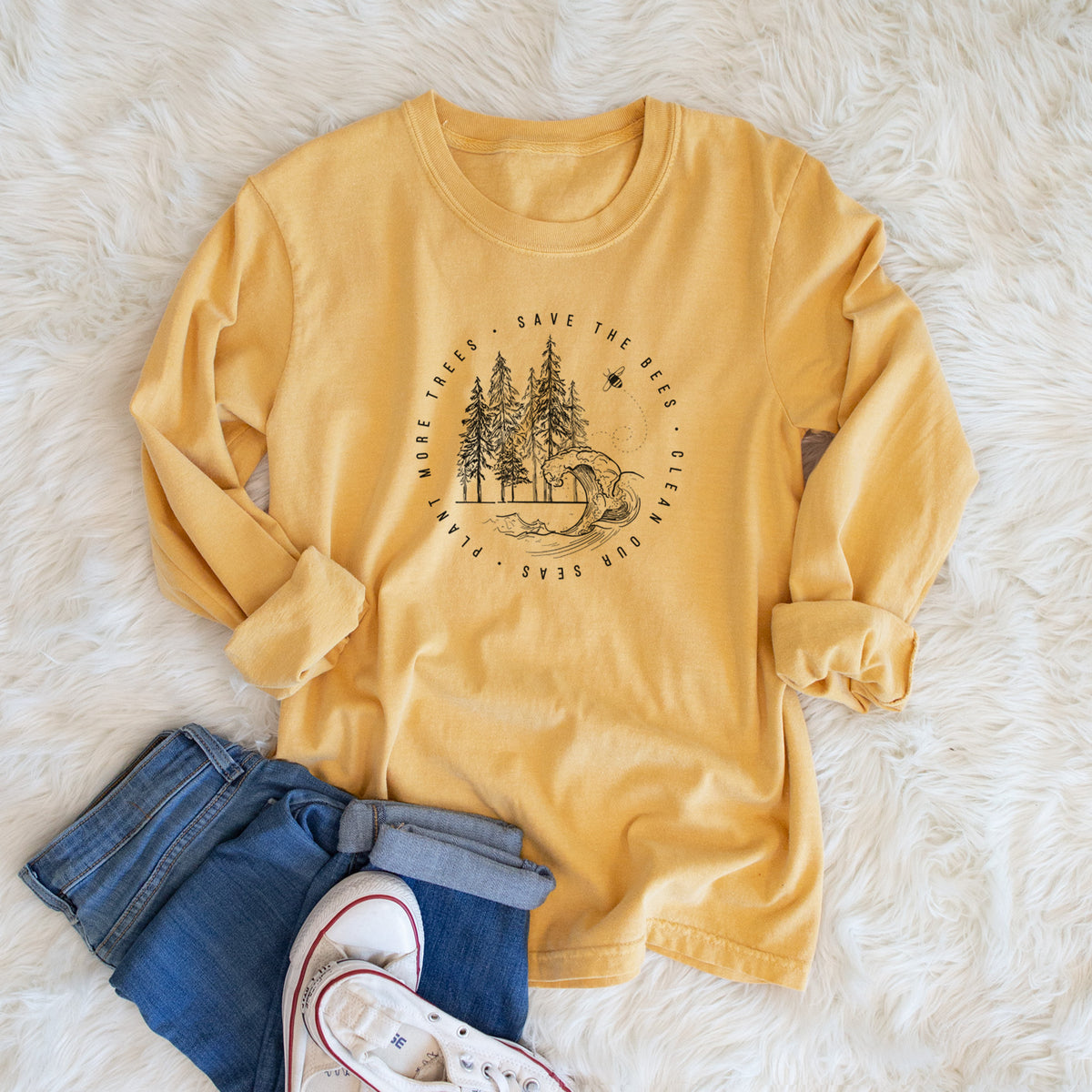 Golden wheat yellow Comfort Colors long sleeve shirt printed with a circle of pine trees and an ocean wave ringed by the words Save the Bees, Clean Our Seas, Plant More Trees, shown in a lifestyle photo.
