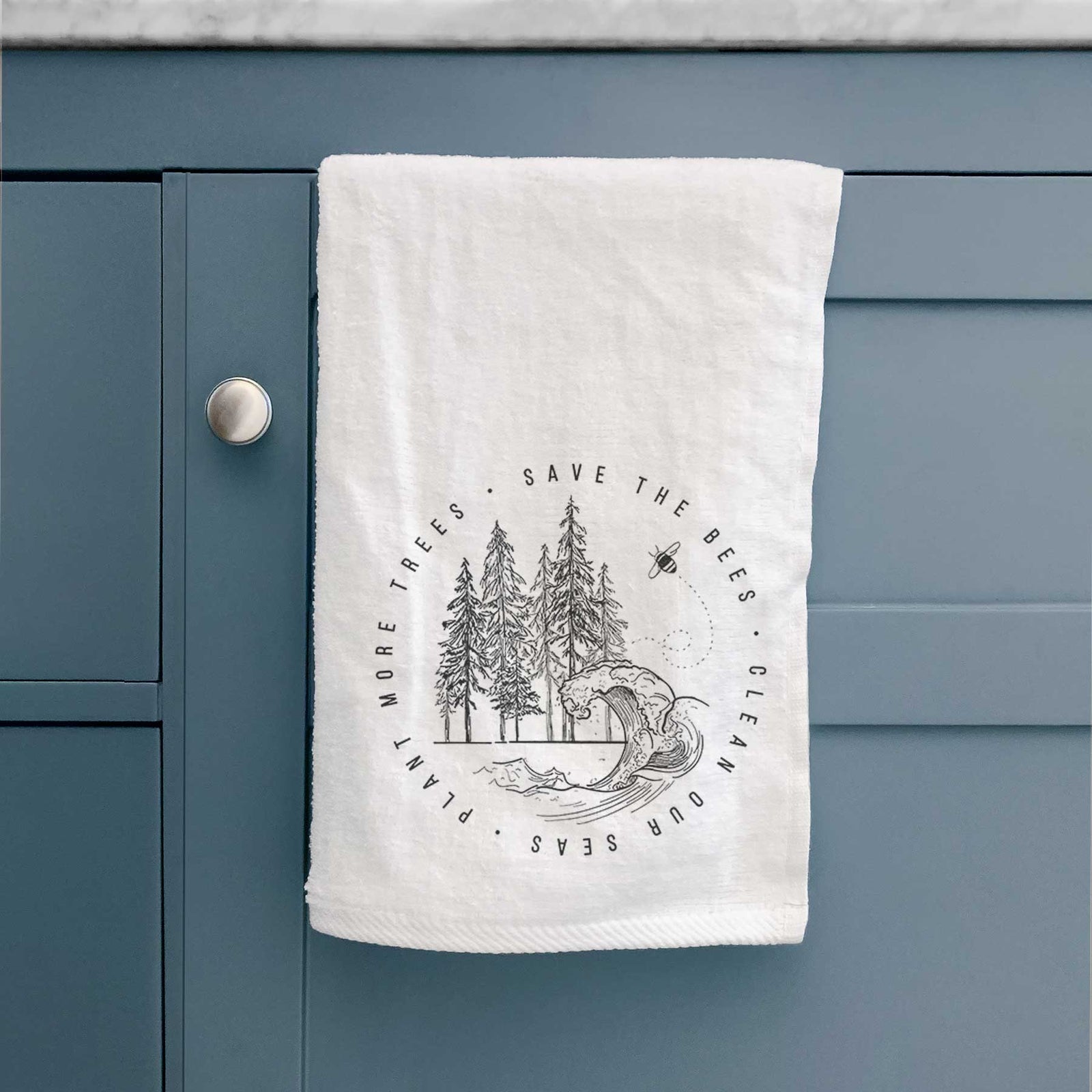 White hand towel printed with a circle of pine trees and an ocean wave ringed by the words Save the Bees, Clean Our Seas, Plant More Trees.