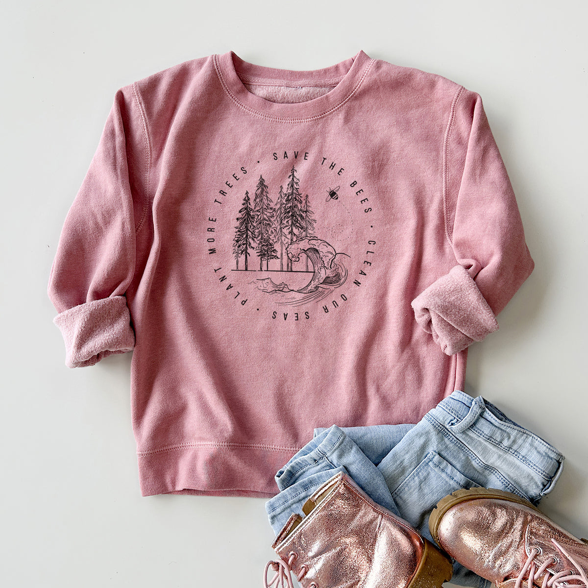 Youth crewneck sweatshirt printed with a circle of pine trees and an ocean wave ringed by the words Save the Bees, Clean Our Seas, Plant More Trees, styled flat with jeans and boots.
