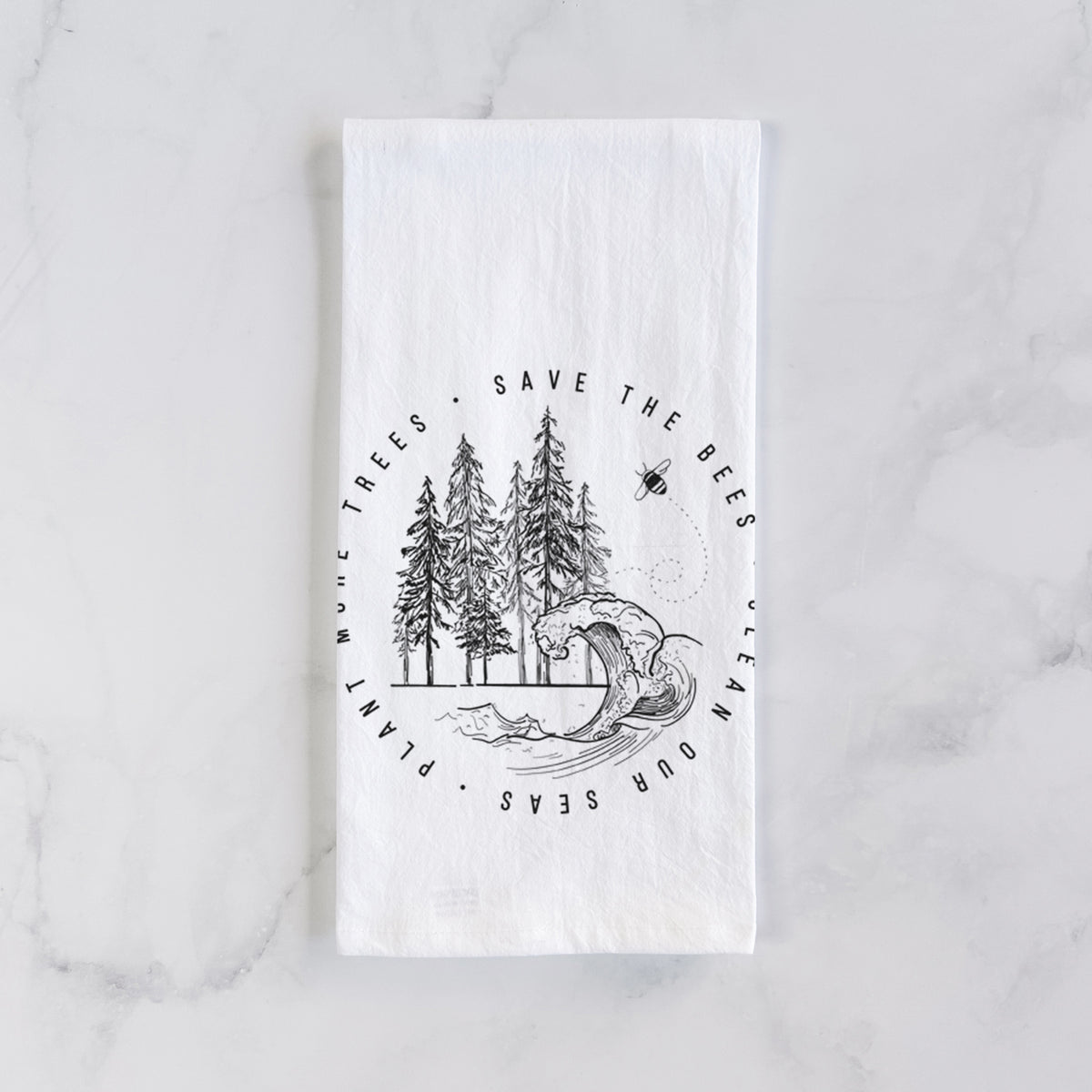 White cotton tea towel laid flat on marble, printed with a circle of pine trees and an ocean wave ringed by the words Save the Bees, Clean Our Seas, Plant More Trees.