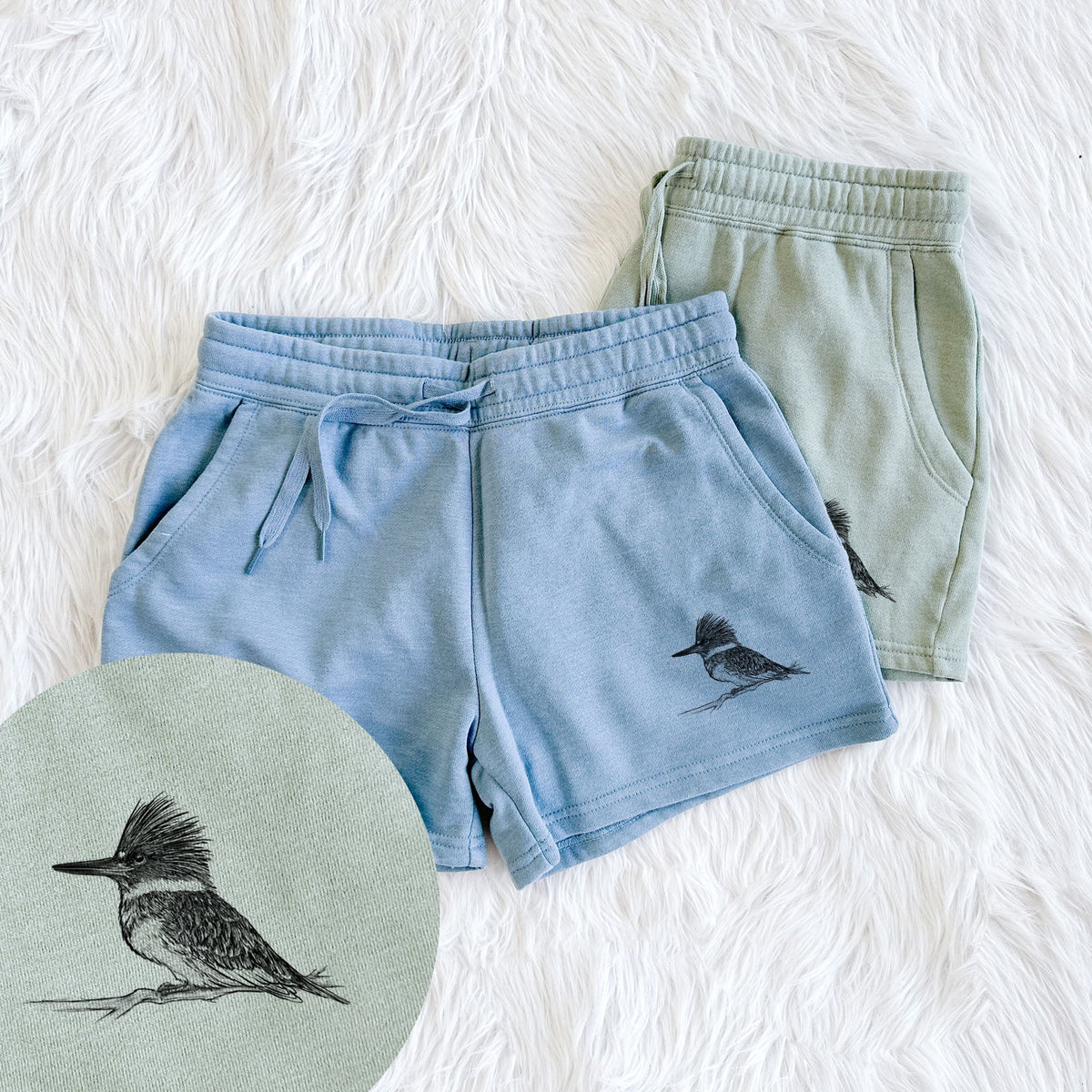 Two pairs of Cali Wave shorts in different colors printed with a detailed black ink sketch of a belted kingfisher perched on a branch, with a close-up of the print.