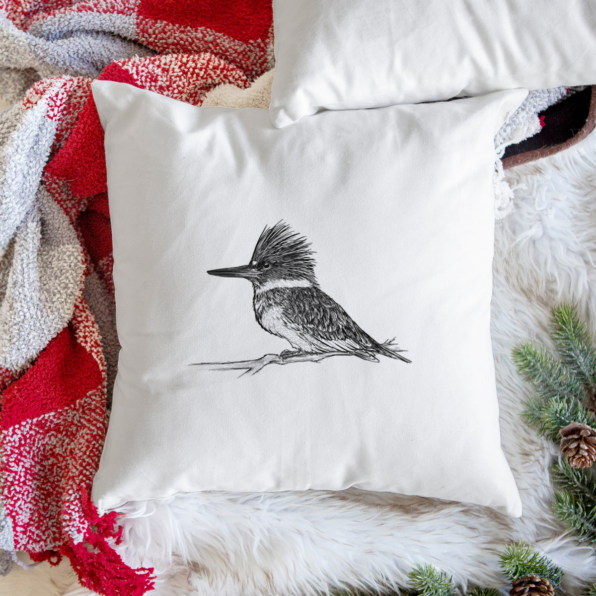 White pillow cover printed with a detailed black ink sketch of a belted kingfisher perched on a branch, on a woven chair.