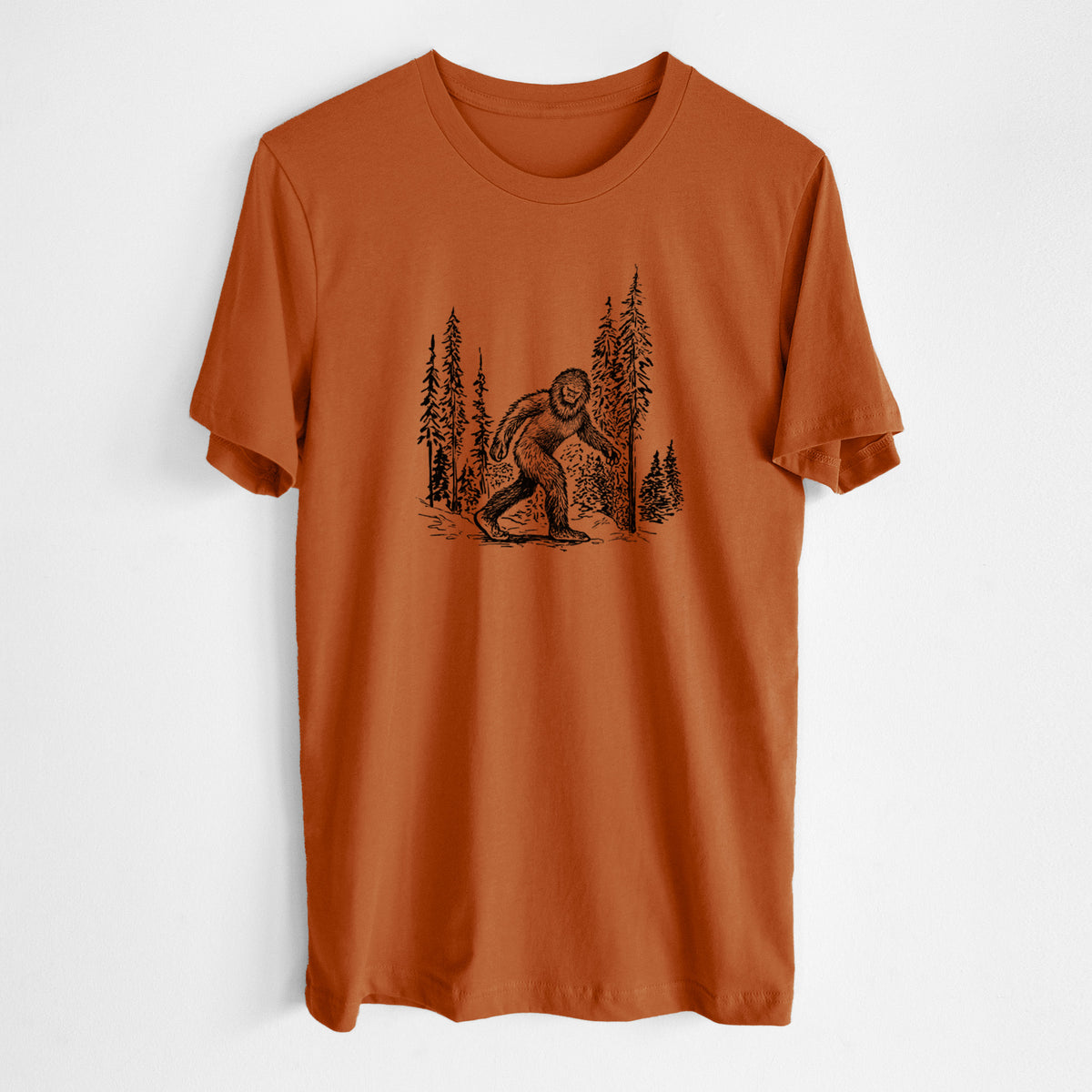Autumn lightweight cotton t-shirt laid flat, printed with a black ink illustration of Bigfoot walking through a pine forest.