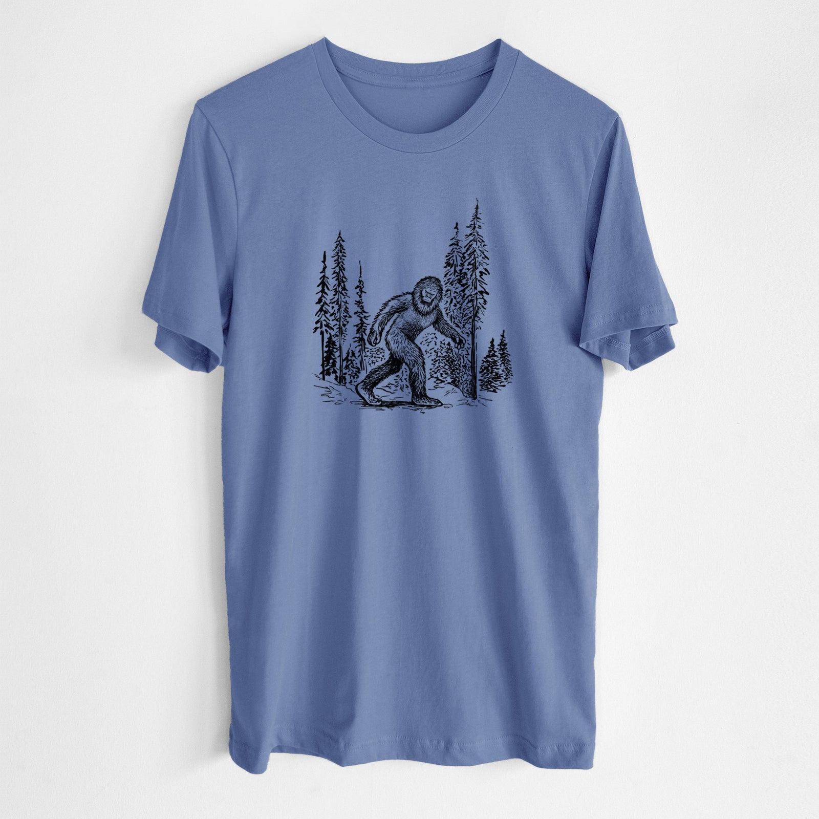 Blue bell lightweight cotton t-shirt laid flat, printed with a black ink illustration of Bigfoot walking through a pine forest.