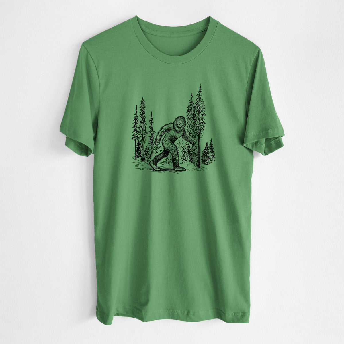 Leaf green lightweight cotton t-shirt laid flat, printed with a black ink illustration of Bigfoot walking through a pine forest.