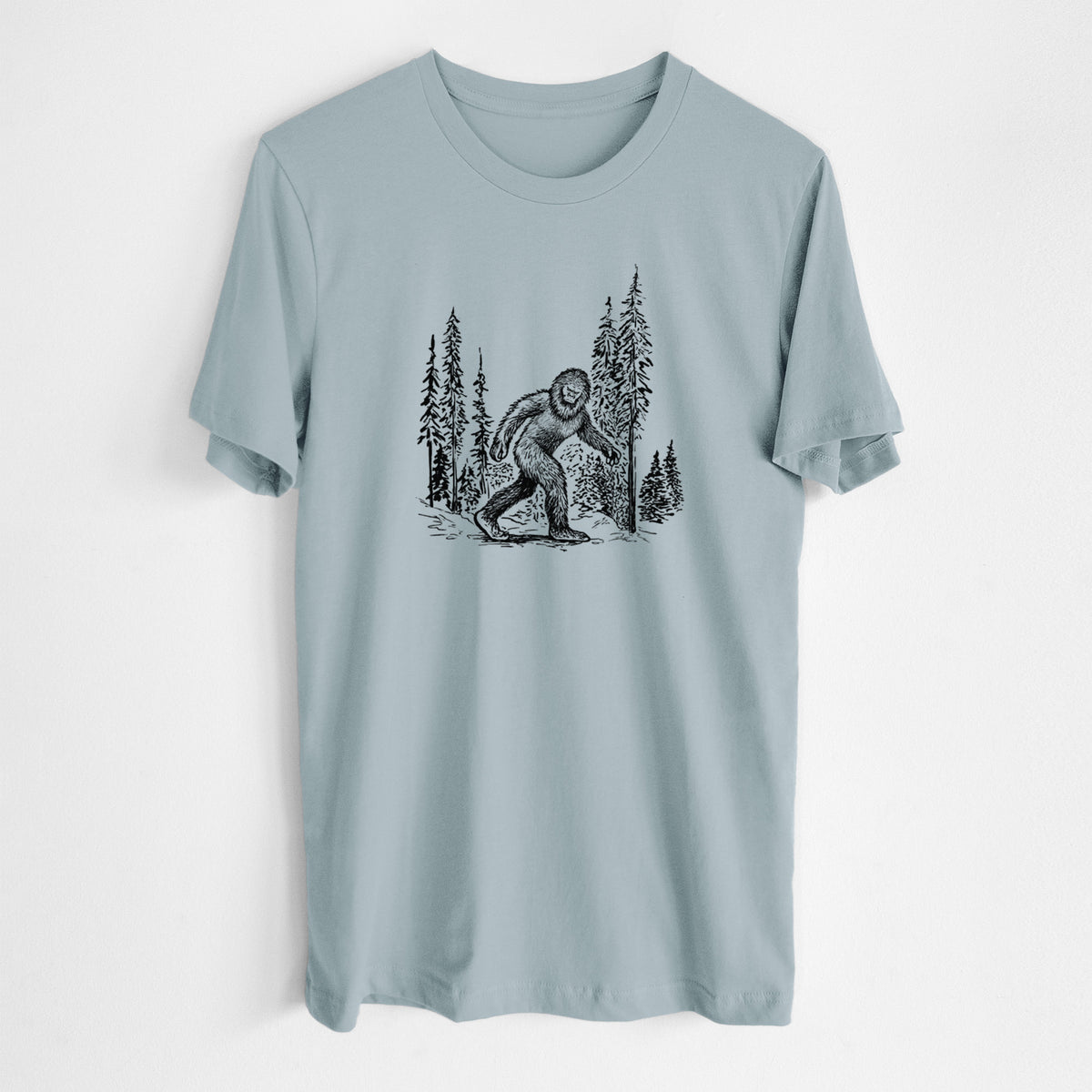 Vintage denim lightweight cotton t-shirt laid flat, printed with a black ink illustration of Bigfoot walking through a pine forest.