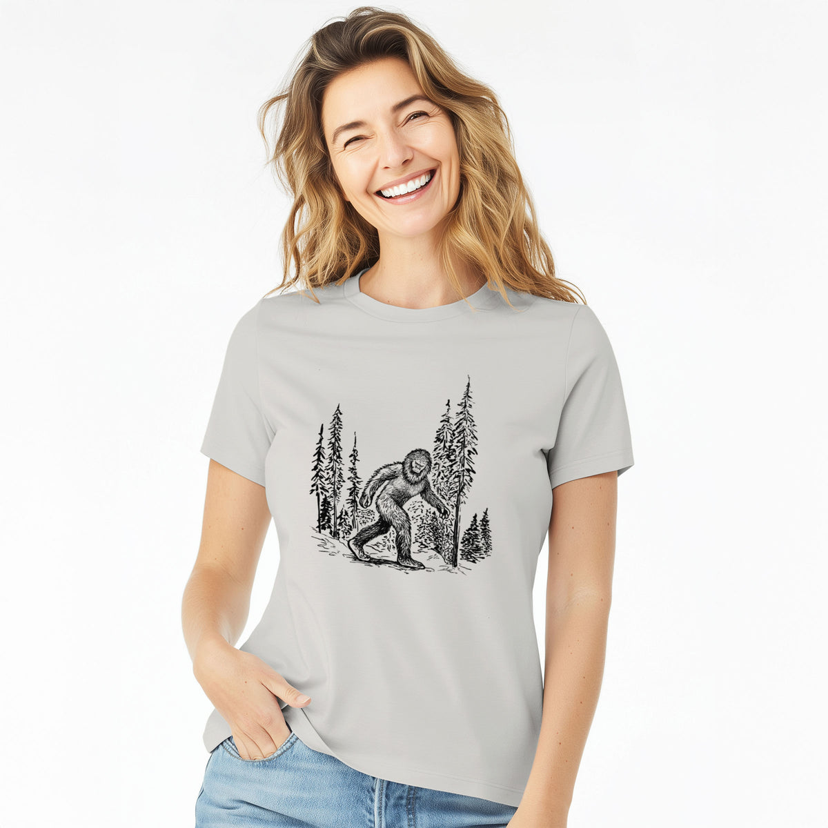 Woman wearing a lunar grey women's relaxed fit cotton t-shirt printed with a black ink illustration of Bigfoot walking through a pine forest.