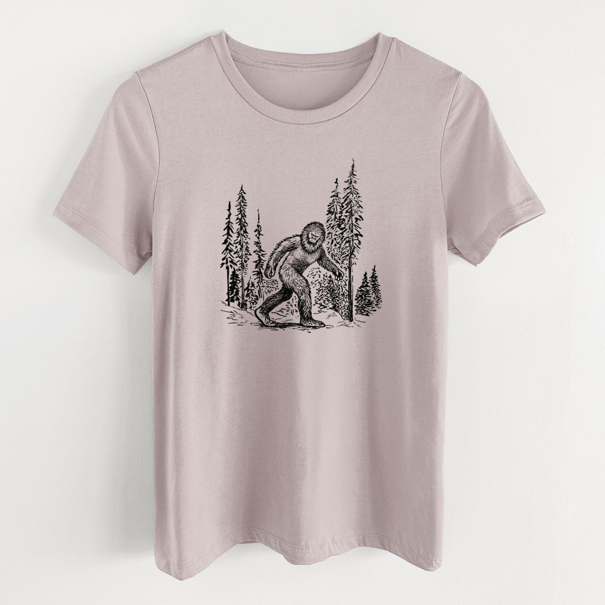 Pink gravel women's relaxed fit cotton t-shirt laid flat, printed with a black ink illustration of Bigfoot walking through a pine forest.