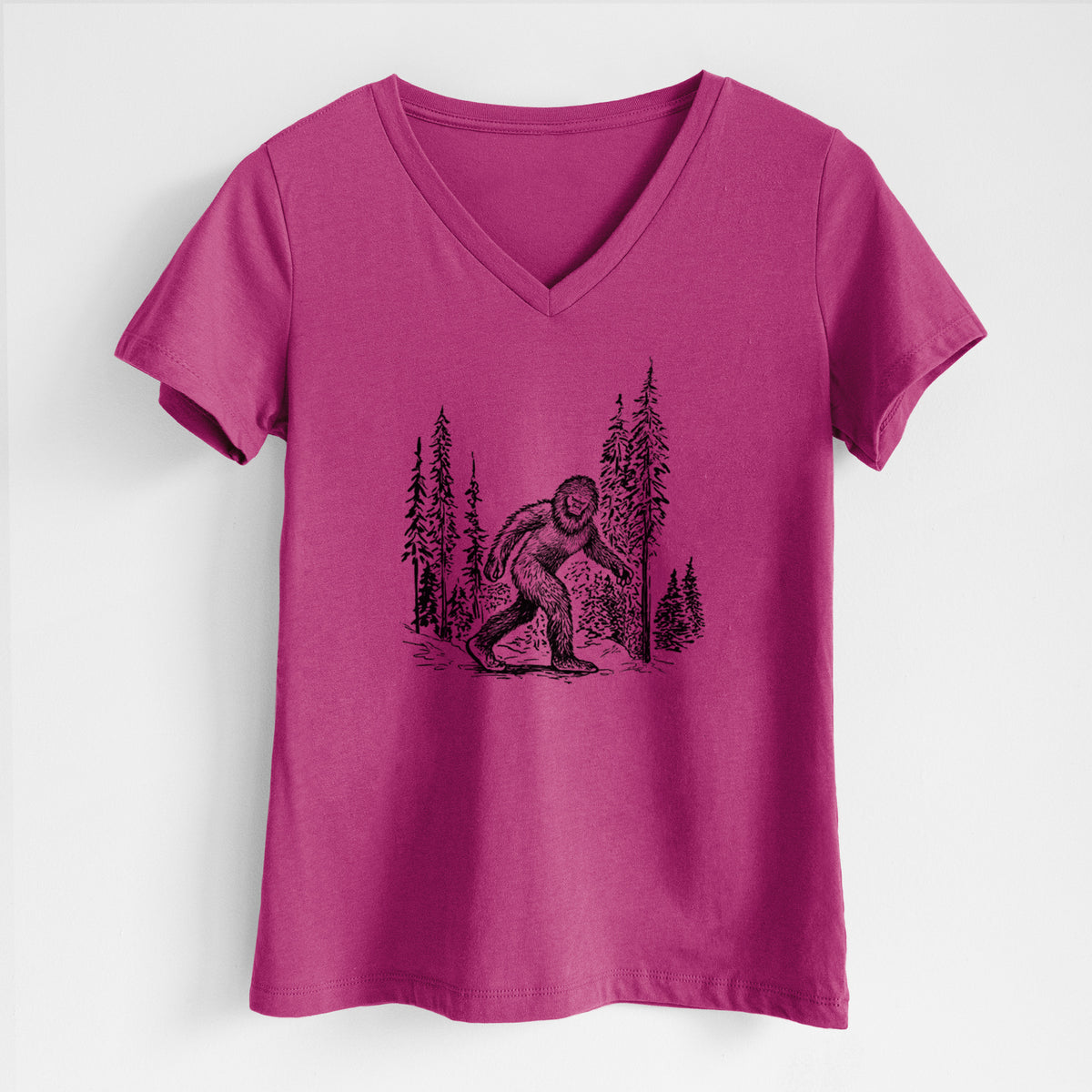 Berry pink women's relaxed fit cotton V-neck t-shirt laid flat, printed with a black ink illustration of Bigfoot walking through a pine forest.