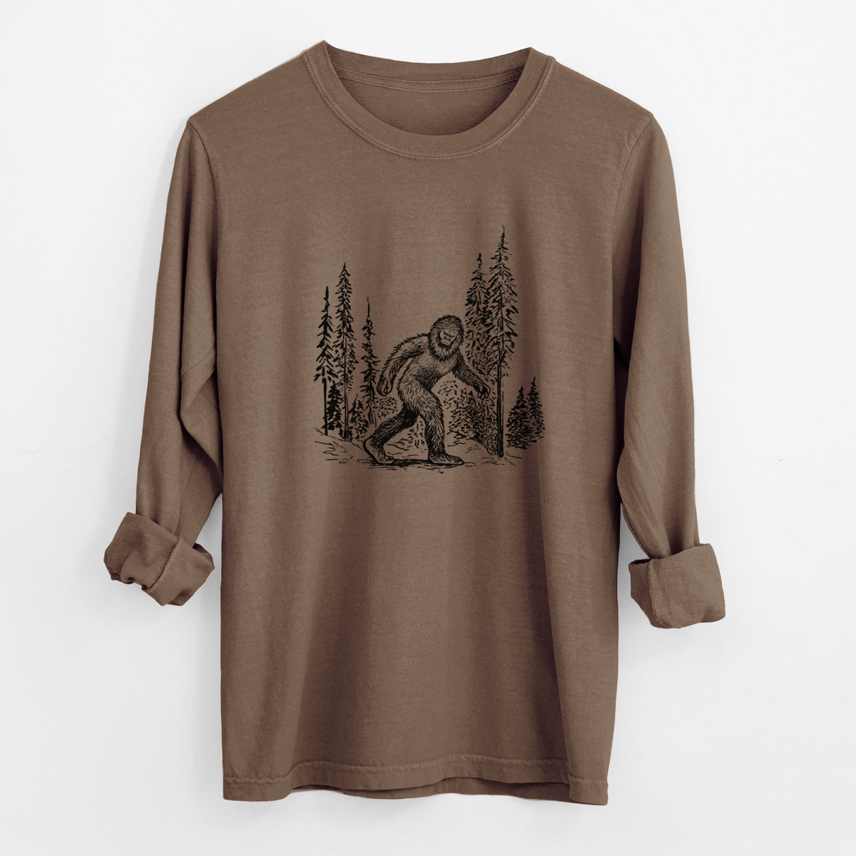 Espresso brown Comfort Colors long sleeve shirt laid flat with the cuffs rolled, printed with a black ink illustration of Bigfoot walking through a pine forest.