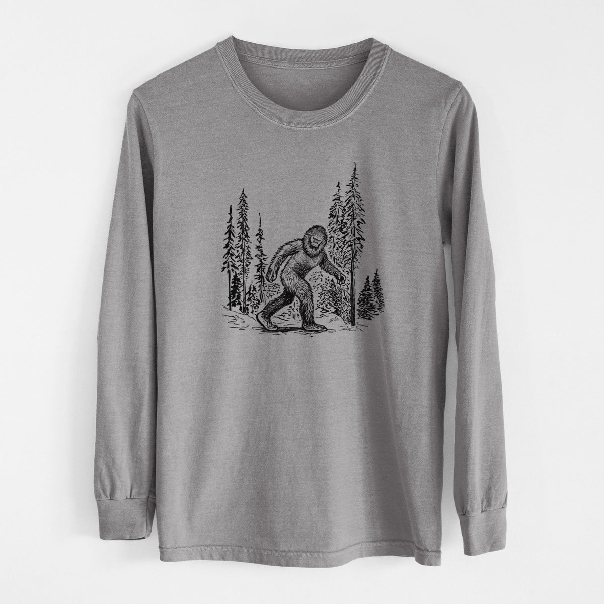 Grey Comfort Colors long sleeve shirt laid flat, printed with a black ink illustration of Bigfoot walking through a pine forest.