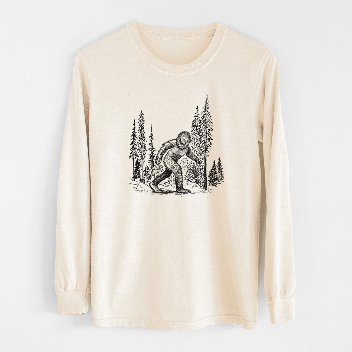 Ivory Comfort Colors long sleeve shirt laid flat, printed with a black ink illustration of Bigfoot walking through a pine forest.