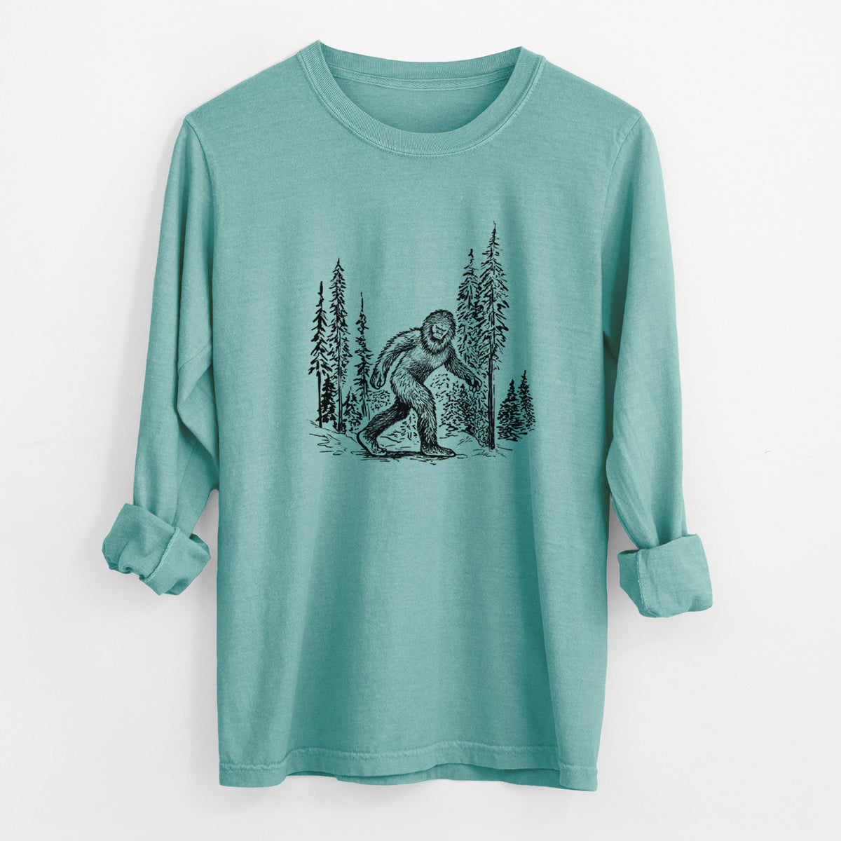 Reef green Comfort Colors long sleeve shirt laid flat with the cuffs rolled, printed with a black ink illustration of Bigfoot walking through a pine forest.