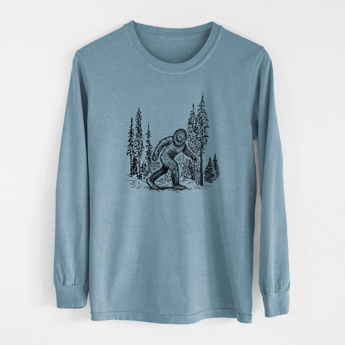 Steel blue Comfort Colors long sleeve shirt laid flat, printed with a black ink illustration of Bigfoot walking through a pine forest.