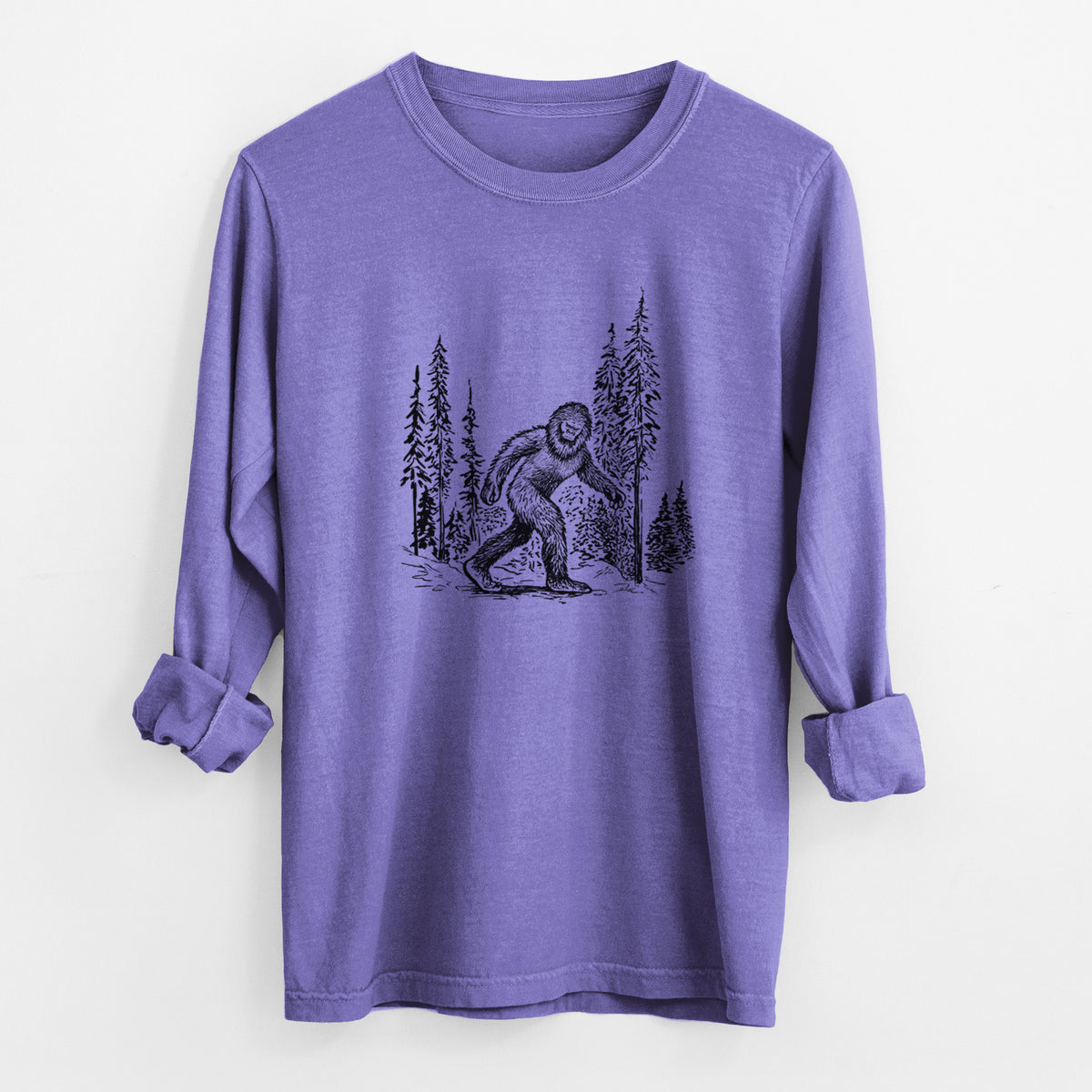 Violet purple Comfort Colors long sleeve shirt laid flat with the cuffs rolled, printed with a black ink illustration of Bigfoot walking through a pine forest.