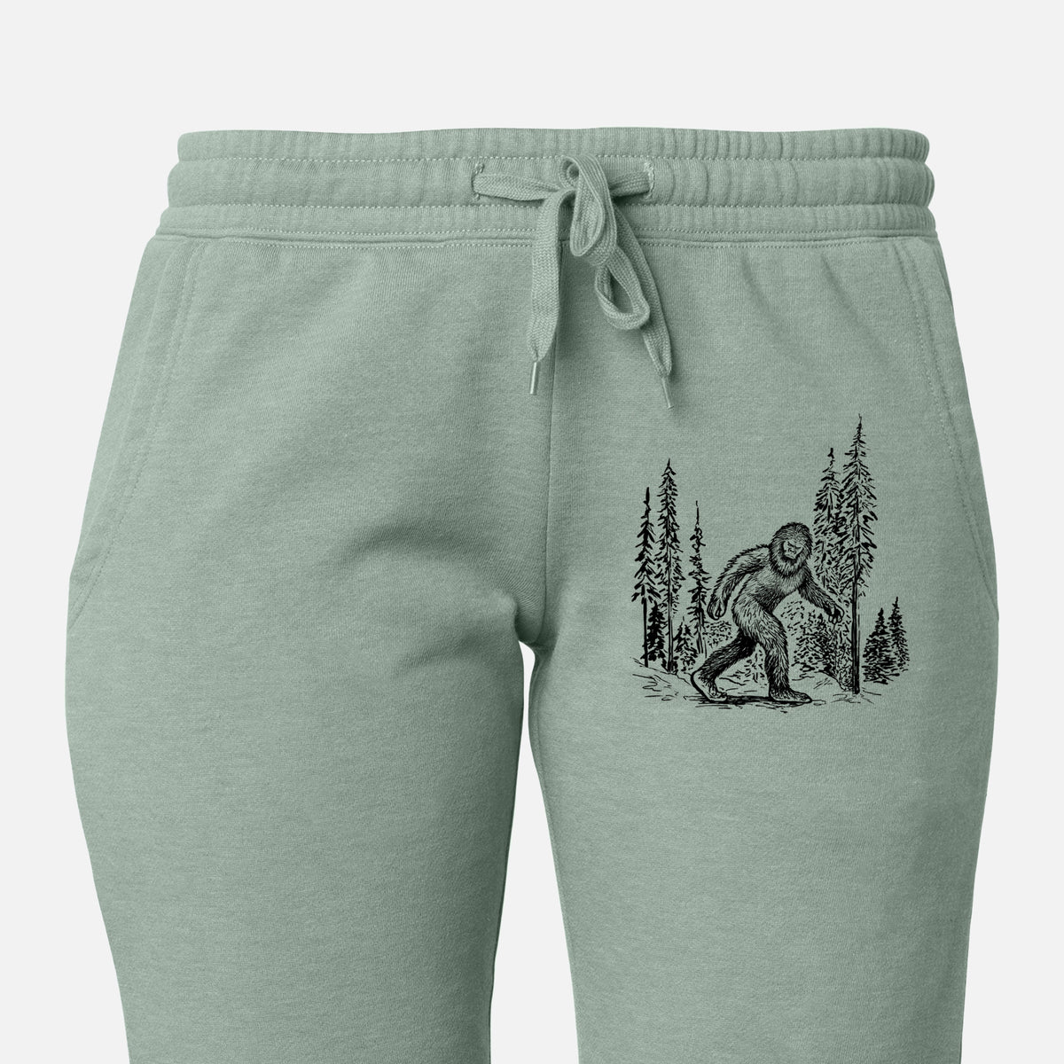 Front of sage green Cali Wave sweatpants, printed with a black ink illustration of Bigfoot walking through a pine forest on the leg.