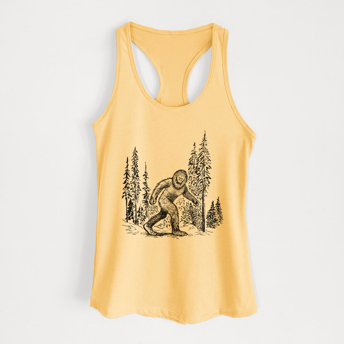 Banana cream women's racerback tank top laid flat, printed with a black ink illustration of Bigfoot walking through a pine forest.
