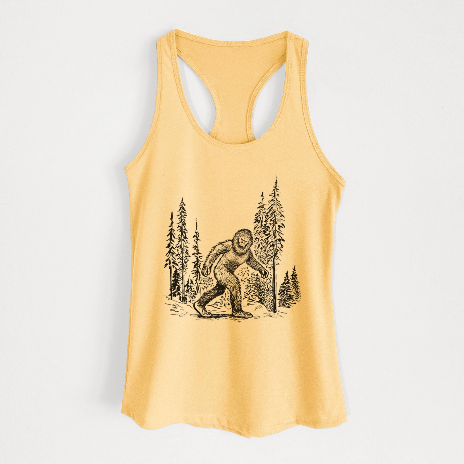 Banana cream women's racerback tank top laid flat, printed with a black ink illustration of Bigfoot walking through a pine forest.