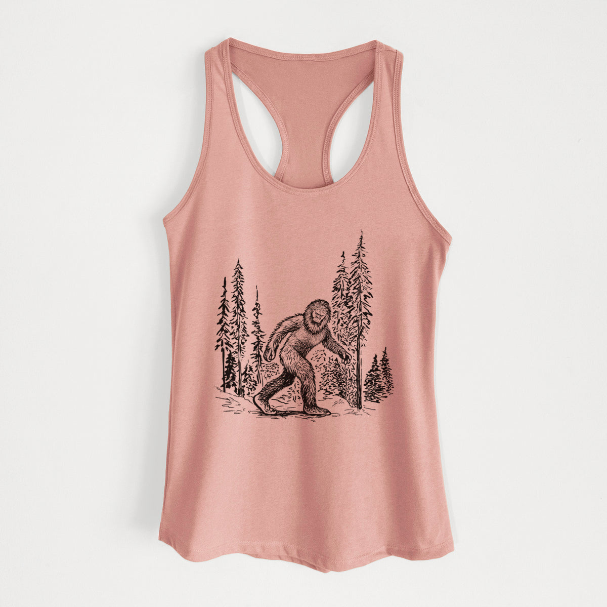 Desert pink women's racerback tank top laid flat, printed with a black ink illustration of Bigfoot walking through a pine forest.