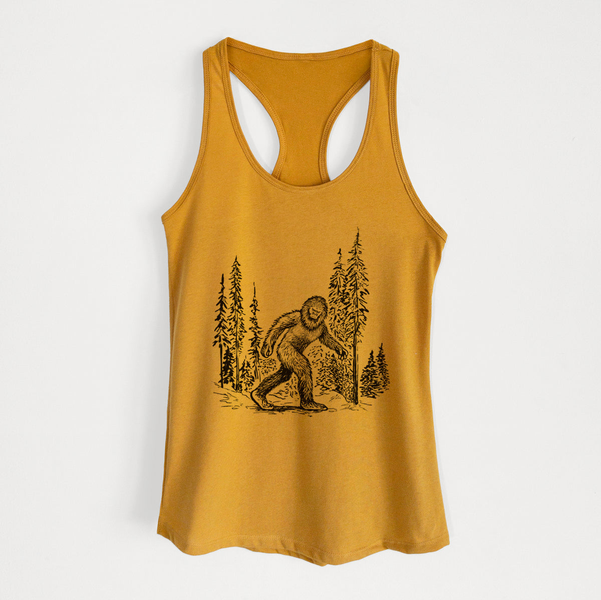 Gold women's racerback tank top laid flat, printed with a black ink illustration of Bigfoot walking through a pine forest.