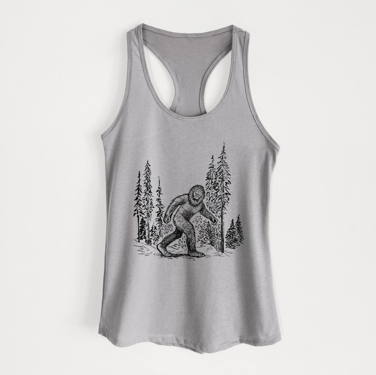 Heather grey women's racerback tank top laid flat, printed with a black ink illustration of Bigfoot walking through a pine forest.