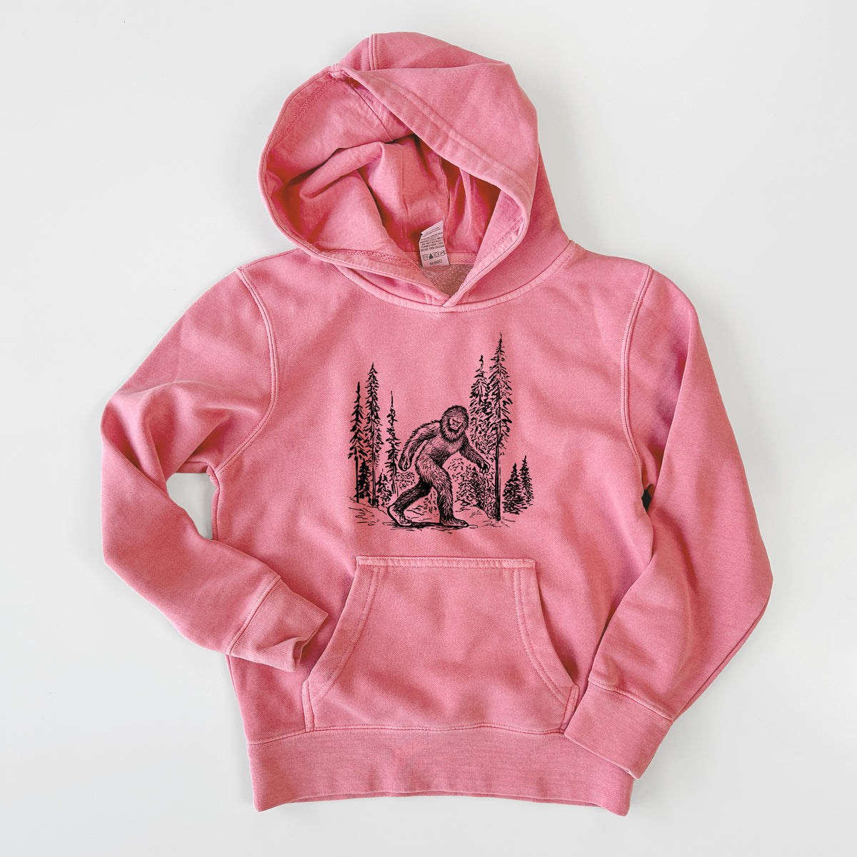 Pigment pink youth pigment dyed hoodie laid flat, printed with a black ink illustration of Bigfoot walking through a pine forest.