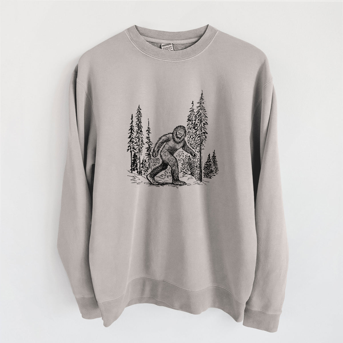Cement grey pigment dyed crewneck sweatshirt laid flat, printed with a black ink illustration of Bigfoot walking through a pine forest.