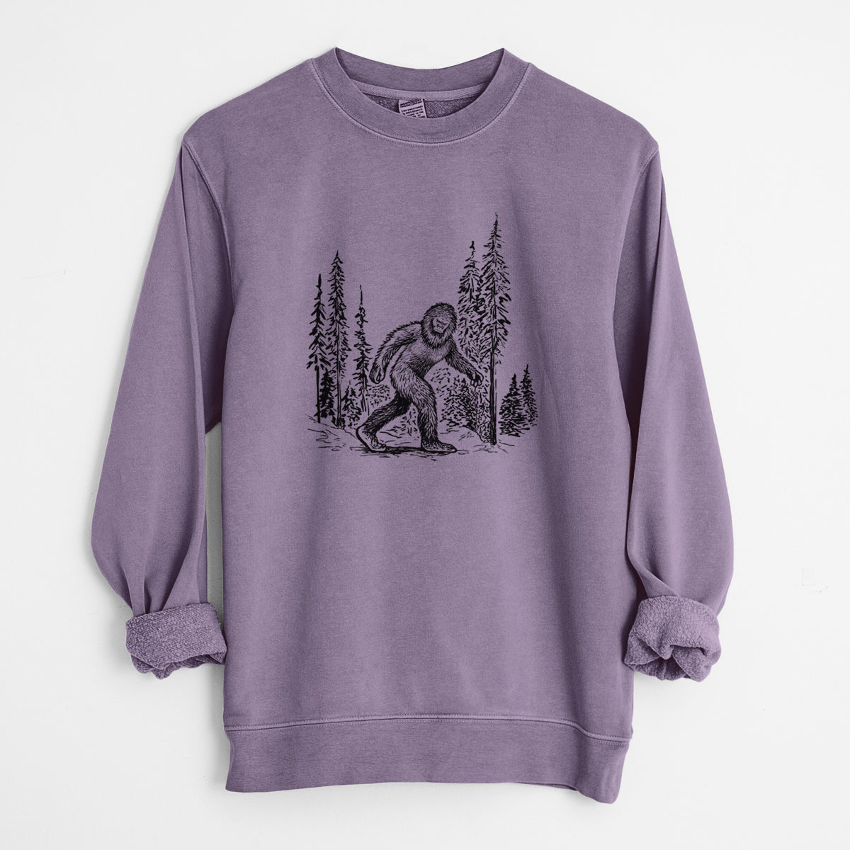 Plum purple pigment dyed crewneck sweatshirt laid flat with the sleeves rolled, printed with a black ink illustration of Bigfoot walking through a pine forest.