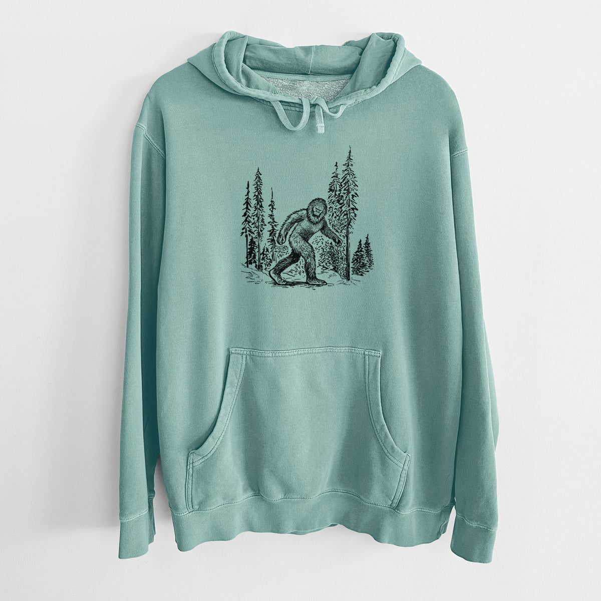 Mint green pigment dyed hoodie laid flat, printed with a black ink illustration of Bigfoot walking through a pine forest.