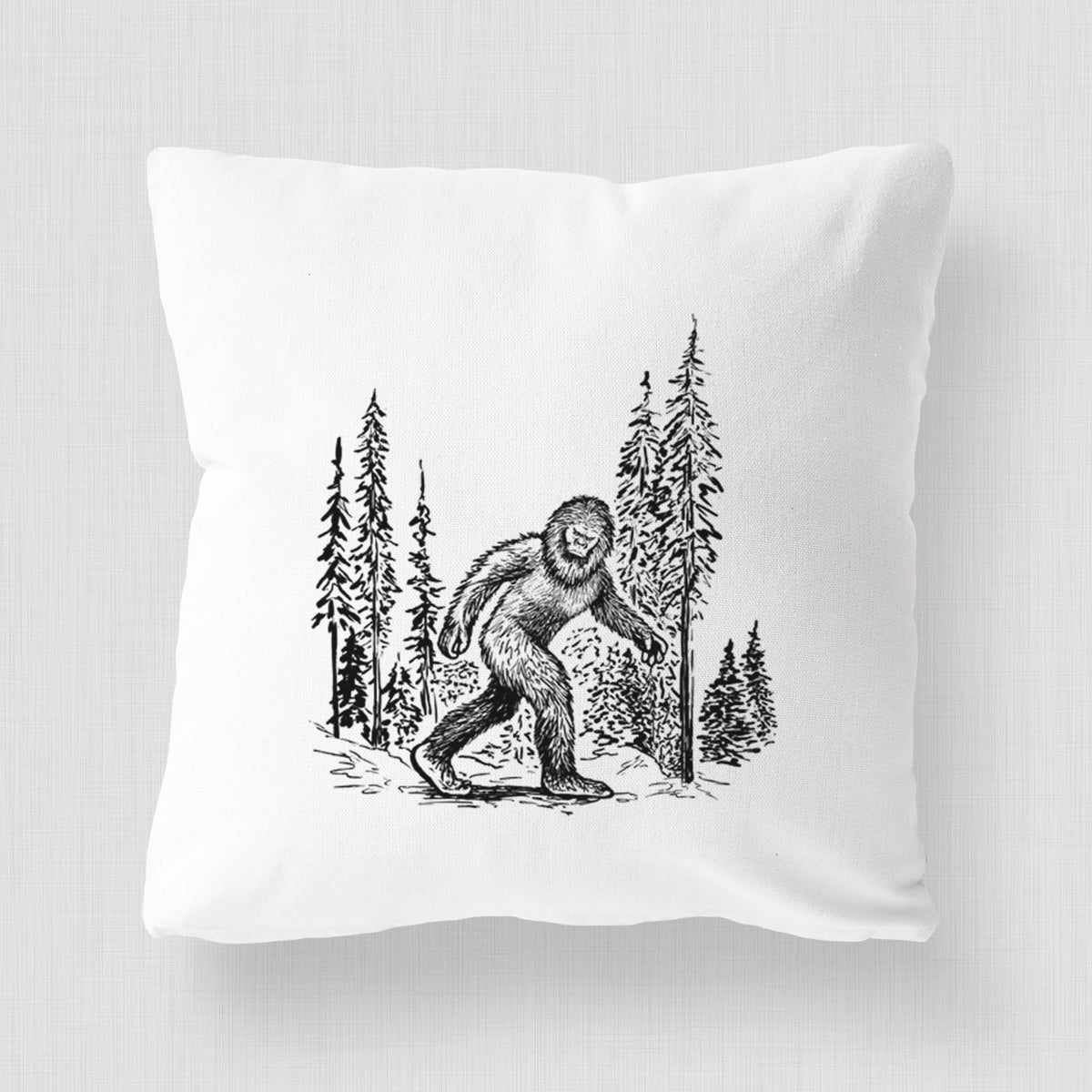 White pillow cover printed with a black ink illustration of Bigfoot walking through a pine forest.